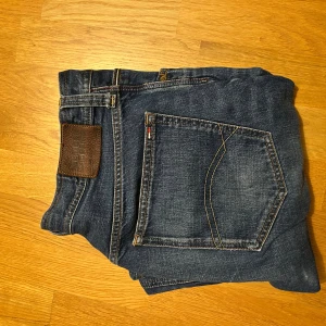 Tommy Hilfiger blå jeans straight fit - Tommy Hilfiger jeans i blå denim med raka ben och normal passform. Perfekta för dig som gillar tidlös stil och vill ha ett par jeans som funkar till allt. Storlek 32/34
