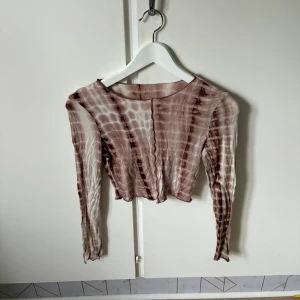 Brun och beige croppad topp från SHEIN - Säljer en croppad långärmad topp från SHEIN i storlek 34. Toppen har ett coolt batikmönster i bruna och beige toner, med vågig kant nedtill och tunn, mjuk polyesterkvalitet. Perfekt för dig som gillar trendiga och unika plagg med lite edge.