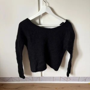 Svart omlottstickad tröja H&M  - Mysig svart stickad tröja från H&M i alpackablandning. Tröjan har lång ärm och snygg omlottdetalj framtill som ger en cool twist. Perfekt för lager-på-lager och passar till både jeans och kjol.