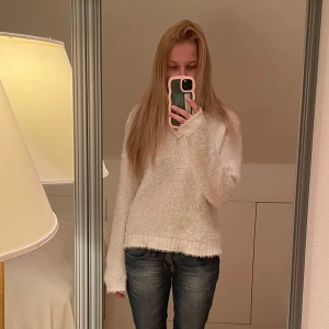 Vit fluffig stickad tröja - Supermjuk och fluffig vit stickad tröja med lång ärm och relaxed fit. Tröjan har en enkel rund halsringning och är perfekt för lager-på-lager. Den är lätt oversized och har en mysig känsla, perfekt för kyliga dagar.