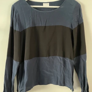 Snygg blå och svart blus från Vila - Säljer en långärmad blus från Vila i blått och svart. Blusen har rund halsringning och dragkedjedetalj i sidan. Materialet känns lätt och luftigt, perfekt för lager-på-lager. Enkel men ändå snygg att styla till jeans eller kjol.