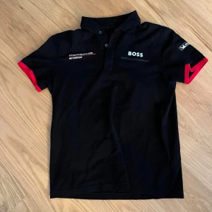 Svart Porsche x BOSS pikétröja M - HELY NY FRÅN MIN PAPPA!! ALDRIG ANDVÄND JÄTTESNYGG SKÖN TRÖJA MYCKET BRA SKICK!! Svart pikétröja från BOSS i samarbete med Porsche Motorsport. Pikén har röda detaljer på ärmsluten, klassisk krage med knappar och tryck på bröstet och ärmen. Perfekt för dig som gillar motorsport och snygg streetstyle.