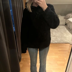 Svart stickad hoodie med huva - Mysig svart stickad hoodie med huva och långa ärmar. Tröjan har en loose passform och är perfekt för kyliga dagar. Materialet är mjukt och värmande, och den enkla designen gör den lätt att matcha med jeans eller andra favoritplagg. Köpt den för 500kr. Helt ny!
