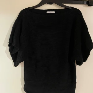 Svart stickad topp från Gina Tricot - Svart stickad topp från Gina Tricot i storlek S. Modellen har breda, korta ärmar och en rund halsringning. Materialet är grovstickat och ger en cool struktur. Perfekt att styla med jeans eller kjol för en chill look.