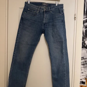 Blå jeans från Dressmann Regular Fit - Snygga blå jeans från Dressmann i modellen Regular Fit. Klassisk femficksdesign med raka ben och normal passform. Jeansen har en mörkblå tvätt och är tillverkade i slitstarkt bomullsmaterial. Perfekt för dig som gillar enkel och tidlös stil.nästan aldrig använda,nypris 700kr