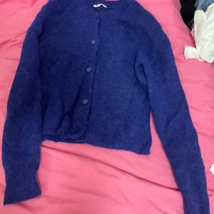 Blå fluffig kofta med knappar - Säljer en mysig blå kofta med rund hals och matchande blå knappar framtill. Koftan har lång ärm och är tillverkad i ett fluffigt stickat material som ger en skön och chill vibe. Perfekt att slänga på sig när det är lite kyligt ute.