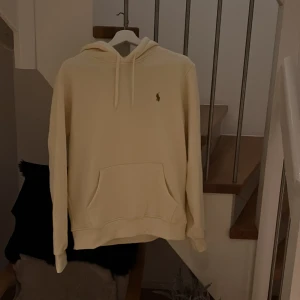 Beige hoodie från Ralph Lauren - Snygg beige hoodie från Ralph Lauren med klassisk broderad logga på bröstet. Tröjan har huva med snörning och en stor magficka framtill. Perfekt för dig som gillar en clean och stilren look. Helt ny oanvänd Storlek L passar mer som en M