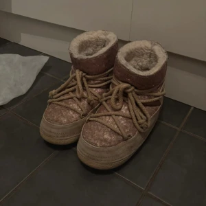 Rosa glittriga Inuikii moon boots - Säljer ett par rosa glittriga Inuikii moon boots med grov snörning och fluffigt foder. Skorna har en platt sula och är perfekta för kalla dagar. Utsidan är täckt av paljetter och insidan är fodrad med mjukt syntetpäls för extra värme.