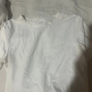 Vit t-shirt från 157, storlek M - En klassisk kroppad vit t-shirt från 157 i storlek M. T-shirten har rund hals och korta ärmar, tillverkad i mjuk bomull som känns skön mot huden. Perfekt för dig som gillar enkel och clean stil. Passar till jeans, shorts eller under en hoodie.