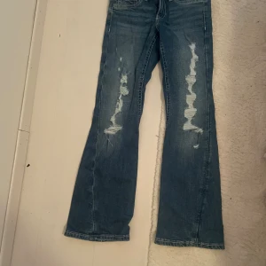 Blå iconic twisted jeans med slitningar - Populära Snygga blå iconic twisted jeans med slitna detaljer framtill och coola fickor med knappar bak. De är lågmidjade och bootcut och slutsålda i de flesta storlekarna. De är HELT oanvända, säljer då de var för små. De är i strl 158
