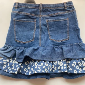 Blå jeanskjol med volang och leopardmönster - Säljer en blå jeanskjol med volangkant och leopardmönstrad underdel i vitt och blått. Kjolen har klassiska jeansdetaljer som fickor fram och bak, bälteshällor och dragkedja. Passar perfekt för mig som är 167cm och volangen syddes på själv alltså finns ej liknande ❤️