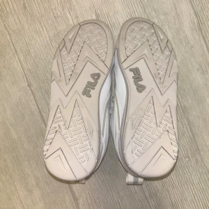 Vita Fila sneakers strl 37 - Säljer ett par vita Fila sneakers i storlek 37. Skorna har chunky sula, snörning och detaljer i syntetmaterial. Klassisk Fila-logga på sidan och tungan, samt dragflik baktill. Perfekta för dig som gillar sportig och clean stil. Helt nya, aldrig använda. 