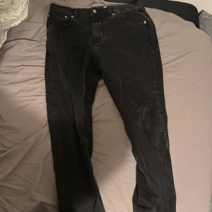 Svarta jeans - Svarta jeans med klassisk femficksdesign och smal passform. Jeansen har silverfärgade nitar och knapp, samt diskreta sömmar. Perfekta för dig som gillar en clean och stilren look.