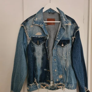 Jeansjacka från Zara - Säljer en cool patchwork jeansjacka från Zara Woman i olika blå nyanser. Jackan har slitna detaljer och bröstfickor med knappar.