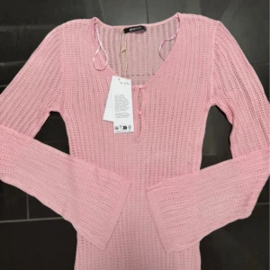 Rosa lång stickad klänning Gina Tricot - Supersöt långklänning från Gina Tricot i ljusrosa stickat material. Klänningen har v-ringning med knappar och snygg ribbad struktur. Långa ärmar och figurnära passform som ger en trendig look. Perfekt för dig som gillar pastell och stickade detaljer.