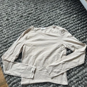 Beige långärmad topp från Gina Tricot - En stilren beige långärmad topp från Gina Tricot, Basically Basics-kollektionen. Toppen har en klassisk rund halsringning och är tillverkad i mjuk bomull, perfekt för en enkel och clean look.