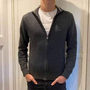 Tommy hillfiger hel zip - Säljer en stilren mörkgrå kofta från Tommy Hilfiger i premium bomull. Koftan har hel dragkedja, ribbade muddar och diskret logga på bröstet. Tröjan har inga defekter och har varit sparsamt använd. Jag är 181 och tröjan sitter lite litet. Vid övriga frågor är det bara att skriva🙌Postar inom 48 timmar📬