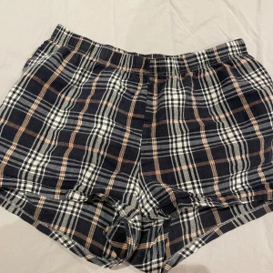 Rutiga shorts - Säljer ett par rutiga shorts med elastisk midja. De har mörk blå, vit och brun färg i ett klassiskt rutmönster. Perfekta för chill dagar eller som pyjamasshorts.