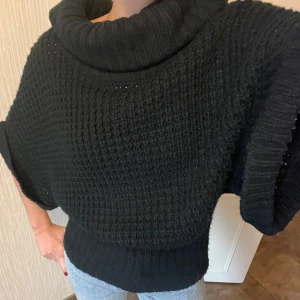 Svart stickad polotröja med kort ärm - Svart stickad polotröja med bred, ribbad krage och korta, vida ärmar. Tröjan har grovstickad struktur och bred ribbad kant nedtill och vid ärmslut. Storlek S, passar även M. Mycket bra skick.