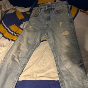Ljusblå slitna Levis 501 jeans - Säljer ett par ljusblå Levis 501 jeans med snygga slitningar och hål på framsidan för en cool, avslappnad look. Klassisk femficksmodell med raka ben och knappgylf. Perfekta för dig som gillar vintagekänsla och streetstyle.