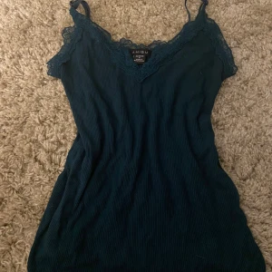 Mörkgrön linnetopp från new Yorker  - Säljer en mörkgrön linnetopp från new Yorker i storlek S. Toppen har spetsdetaljer vid halsringningen och tunna axelband. Materialet är mjukt och stretchigt, perfekt för dig som gillar en slim passform. Snygg volangkant nedtill.