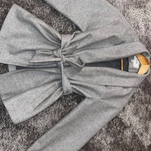 Grå omlott kappa från Vila - Snygg grå kappa från Vila med omlottmodell och bälte i midjan. Jackan har lång ärm, klassisk krage och en stilren look som passar perfekt till höst och vinter. Materialet är mjukt och känns lyxigt, och färgen är neutral vilket gör den enkel att matcha.Storleken är 38 men passar även perfekt för dem som är storlek 36 då jag själv bär storlek 36