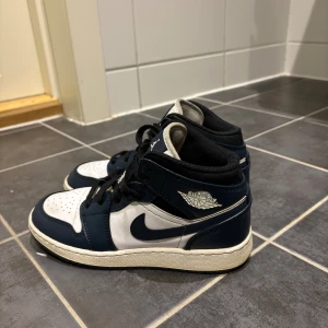 Nike Air Jordan 1 Mid Marinblå/Vit - Säljer ett par Air Jordan 1 som inte användes på fler flera år köptes på gamla restock för 2700. Väldigt fina skor bra skick, minns att de inte användes länge alls. Enda negativa är att ena sulan har gått sönder lite inget som märks! Storlek 35,5! Är lite större i storleken. Pris kan diskuteras vid SNABB affär!