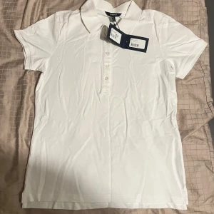 Vit klassisk piké från GANT - Vit pikétröja från GANT med klassisk krage och korta ärmar. Tröjan har tre knappar framtill och diskret broderad logga på bröstet. Tillverkad i mjuk bomull som känns skön mot huden. Perfekt för en clean och stilren look. Till Dam