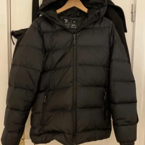 Svart pufferjacka från Neomondo XS - Svart pufferjacka från Neomondo i storlek XS. Jackan har huva, två sidofickor med dragkedja och elastiska muddar vid ärmslut. Materialet är syntet och jackan har en clean, quiltad look med diskret logga på ärmen. Perfekt för kalla dagar. Orginal Pris: 700kr , priset kan samt diskuteras 