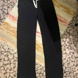 Svarta mjukisbyxor med snörning, M - Svarta mjukisbyxor från R i storlek M. Byxorna har en rak passform och vit snörning i midjan för justering. Tillverkade i mjukt bomullsmaterial som är skönt mot huden. Perfekta för chill eller träning.