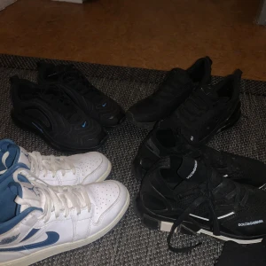 Nike och Dolce & Gabbana sneakers - Flera par sneakers till salu: vita och blå Nike Jordan 1 med klassisk design, svarta Nike Air Max och svarta Dolce & Gabbana sneakers med tydlig logga. Alla har snörning och platt sula. Perfekta för dig som gillar streetstyle och sportig look.
