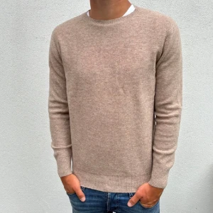 Beige kashmirtröja med rund hals - Snygg beige kashmirtröja med rund hals och ribbade muddar. Tröjan har en clean och klassisk look, perfekt för dig som gillar stilrena plagg. Långärmad och mjuk, passar dig som vill ha något bekvämt och ändå se fräsch ut.