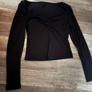 Svart långärmad topp med v-ringning - Snygg svart långärmad topp med v-ringad hals och lätt rynkning framtill. Modellen är figurnära och passar perfekt till jeans eller kjol. Materialet känns mjukt och stretchigt, vilket gör den bekväm att bära hela dagen. Spets vid v ringningen