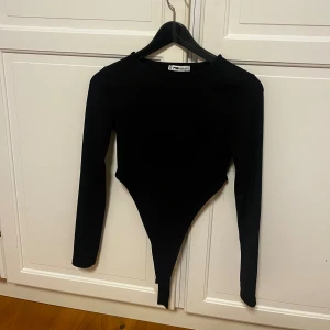Svart ribbad body med höga kanter  - Svart långärmad body med höga kanter vid höften från Sister i storlek XS. har ett ribbat tyg som ger en snygg struktur. Perfekt att styla med höga jeans eller kjol för en trendig look.