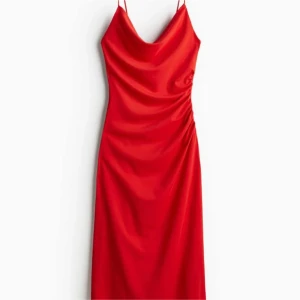 Röd långklänning med smala axelband - Säljer en röd långklänning med smala axelband och snygg drapering vid sidan. Klänningen har en mjuk, glansig yta och en elegant v-ringad hals. Perfekt för dig som vill sticka ut med en stilren look.
