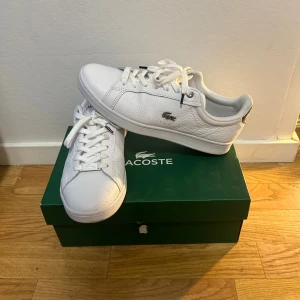 Vita sneakers från Lacoste - Snygga vita sneakers från Lacoste med klassisk krokodillogo på sidan. Har använt skorna max 3-4 gånger, original pris: 1300, mitt pris: 399, kvitto finns!