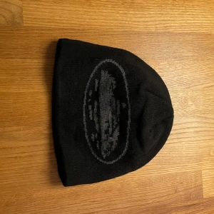 Svart Corteiz mössa - En svart Corteiz mössa med grått märke. Sitter skönt på huvudet och är perfekt för kalla dagar och passar till de flesta outfits.
