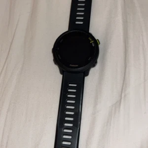 Garmin Forerunner 55 svart sportklocka - Säljer en svart Garmin Forerunner 55 sportklocka med rund urtavla och silikonarmband. Klockan har flera knappar på sidorna och detaljer i silver och neongult. Perfekt för dig som gillar att hålla koll på träningen och vill ha en stilren och funktionell accessoar.