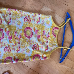 Blommig sommarklänning från H&M - Söt kortklänning från H&M med blommigt mönster i gult, rosa och vitt. Klänningen har smala axelband och ärmlös design, perfekt för varma dagar. Materialet är mjuk bomull och den har en färgglad, lekfull stil som sticker ut.