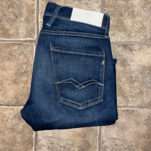 Replay Anbass jeans  - Mörkblå Replay Anbass jeans i slim fit med klassisk femficksdesign och kontrastsömmar. Tillverkade i stretchig jeanskvalitet för skön passform. Midja 38cm, längd 104cm. JAG SKICKAR EJ FLER BILDER NÄR JAG BÄR JEANSEN! för storleksguide hänvisar jag till måtten och för bättre inblick i passformen rekommenderar jag att googla på modellnamnet. Jeansen kan vara uppsydda utan att jag noterat det så kolla måtten noggrant :) s4