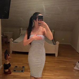 Randig tubklänning i vitt och svart - Säljer en tight, axelbandslös tubklänning med svarta och vita horisontella ränder. Klänningen är midilång och har en kroppsnära passform. Perfekt för dig som gillar en enkel men snygg look. Materialet känns stretchigt och bekvämt.