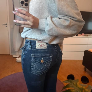 True Religion blå bootcut jeans - Säljer ett par snygga blå jeans från True Religion med ikoniska kontrastsömmar och detaljerad ficka med knapp bak. Modellen har låg midja och bootcut.