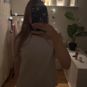 Beige stickad tröja med pärlor från Zara - Supersöt beige stickad tröja från Zara med korta ärmar och rund hals. Tröjan är dekorerad med pärlor framtill som ger en extra touch. Ribbad kant vid halsen och mjukt material som känns skönt mot huden. Lite kort. Aldrig använd. Rätt så högt nypris.