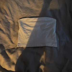 Vit bandeau tubtopp från Gina Tricot - Säljer en enkel och fräsch vit bandeau tubtopp från Gina Tricot i storlek xxs. Toppen är ärmlös och har en rak, tight passform som sitter snyggt över bröstet. Materialet är mjuk bomull med lite stretch för extra komfort. Perfekt för varma dagar och snygga outfits.