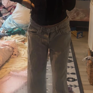 Grå wide jeans med låg midja - Säljer ett par gråa jeans med låg midja och breda ben. Modellen har klassiska fem fickor och knappgylf. Jeansen har en avslappnad passform och är tillverkade i jeansmaterial. Perfekt för dig som gillar en loose och trendig stil.