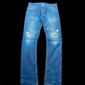 Blå jeans från jack & jones - Säljer ett par blå jeans med slitningar och trasiga detaljer på låren. Jeansen har en klassisk femficksdesign. Materialet är denim och färgen är mellanblå med ljusare tvättade partier. Perfekta för en avslappnad och trendig look. Waist 42cm, Full length 102cm