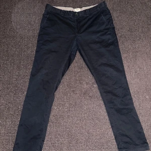 Svarta chinos East West (Brothers) - Snygga svarta chinos från East West i modell Bowery slim fit, storlek W36 L32. Perfekt skick utan tecken på användning. Köpt i Brothers butik. 98% bomull och 2% elastan för en skön stretchig känsla. Klassisk design med knapp och dragkedja framtill samt sidfickor. Perfekta för en clean och stilren look.