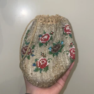 Blommig pärlväska - Väskan är broderad med pärlor och har inte synliga skador. Väskan är 16cm lång