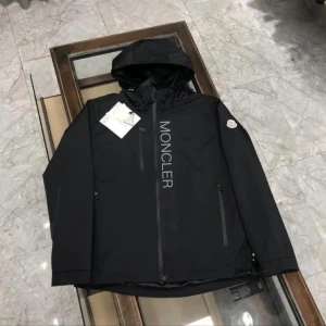 Moncler windbreaker - Svart vindjacka från Moncler med huva och dragkedja framtill. Jackan har Moncler-logga på ärmen och stor vertikal Moncler-text på bröstet. Flera praktiska fickor med dragkedja och justerbara ärmslut. Perfekt för dig som gillar stilren och sportig look.