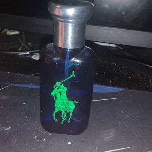 Ralph Lauren blå parfymflaska - Snygg blå parfymflaska med den klassiska Ralph Lauren-loggan och en stor gul etta på framsidan. Perfekt för dig som gillar stilrena och sportiga detaljer. Volym och ingredienser framgår ej på bilderna.